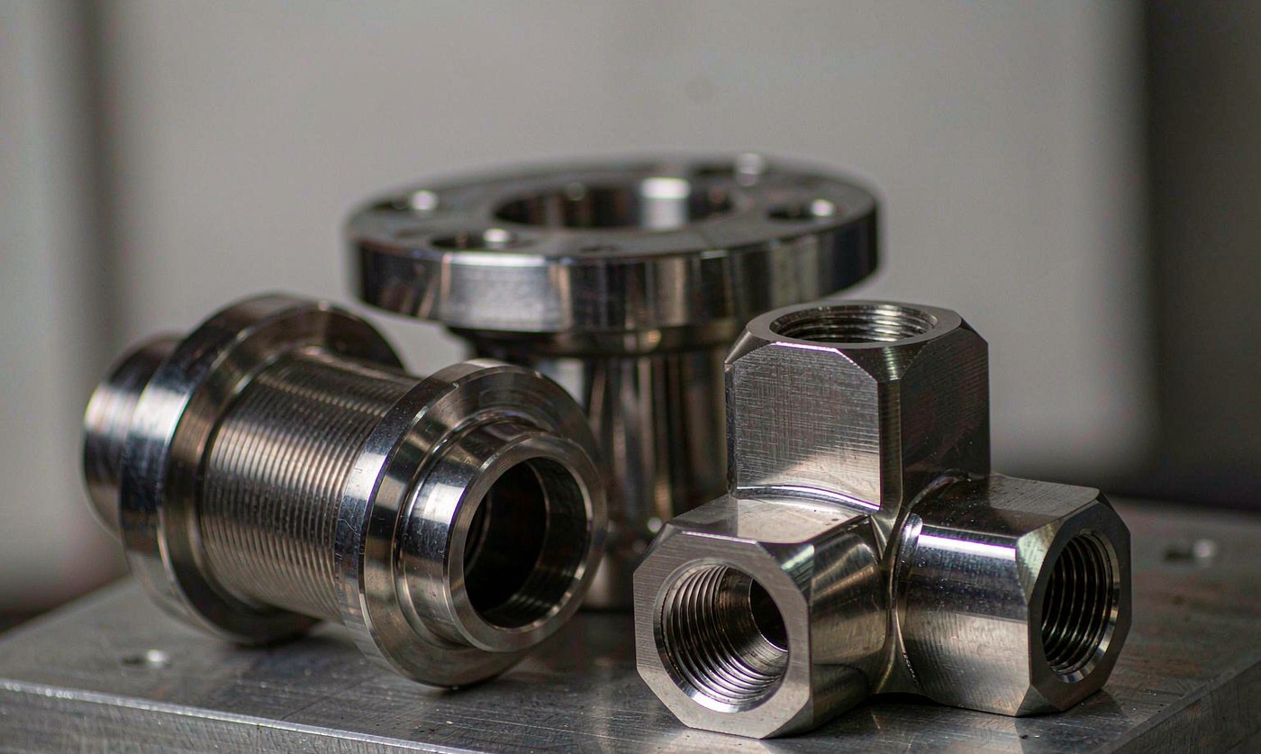 CNC machined 316L stainless steel parts: instrument tee fitting, threaded sensor body and polished flange on a fixture plate